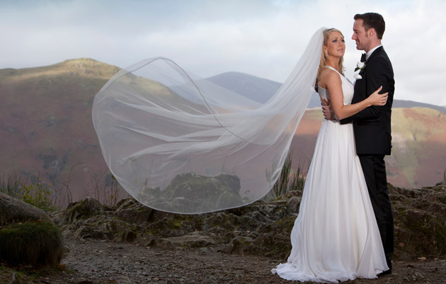 Bride and Groom on a hill with wedding veil caught in the wind