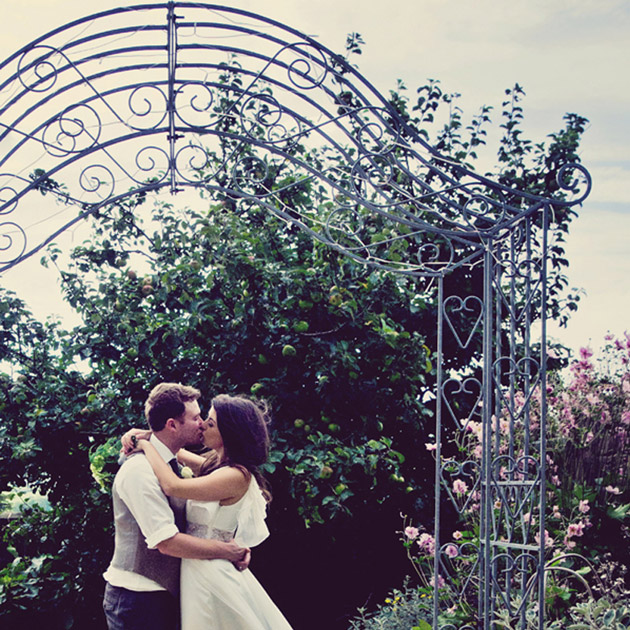 Bride and groom embrace in front of intricate metal arch