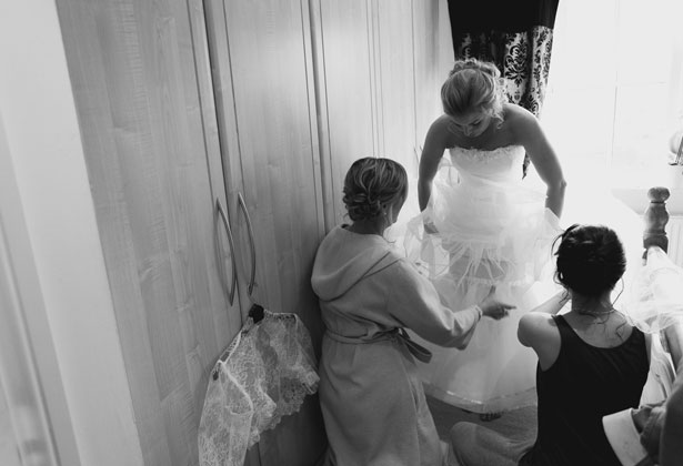 Bridesmaids helping bride in to her dress 