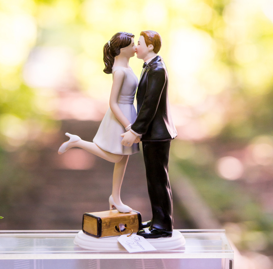 "A Kiss And We're Off!" Figurine - Light Skin Tone - Bride Standing on Suitcase to Kiss the Groom - Unique Cake Topper | Confetti.co.uk