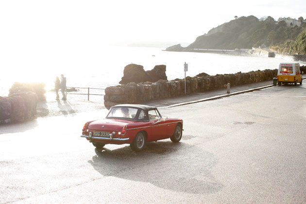 The bride and groom heading to the reception in a red vintage car 