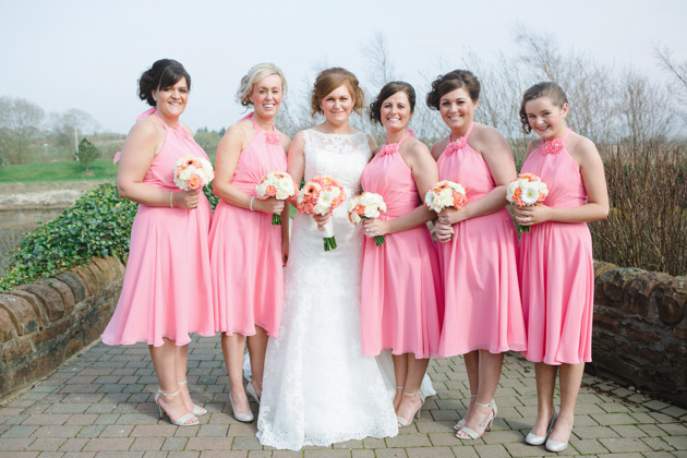 Bridesmaids in coral pink knee length dresses with a draped halter neck