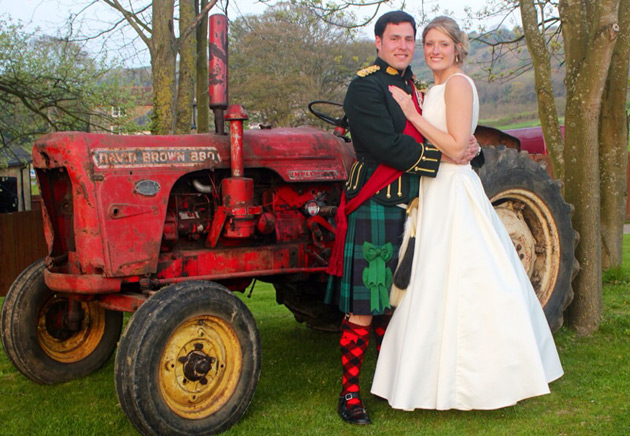 The bride and groom standing next to a red tractor 