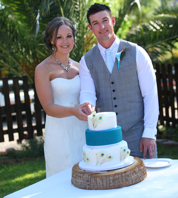 Bride and groomcutting their white and blue peacock feathered wedding cake