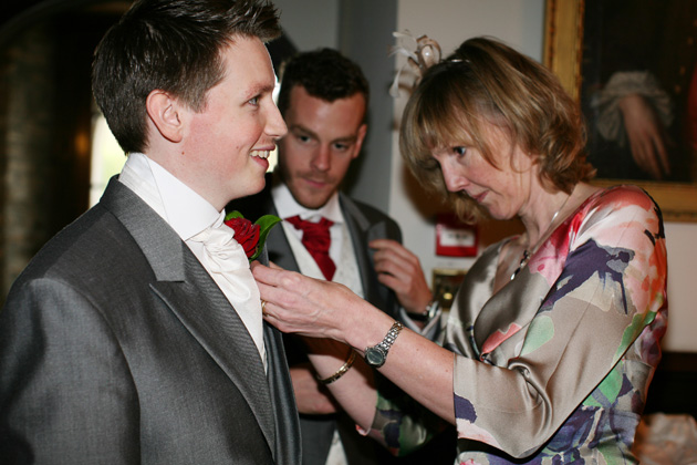 Mother of the groom pinning a red rose button hole on his suit | Confetti.co.uk