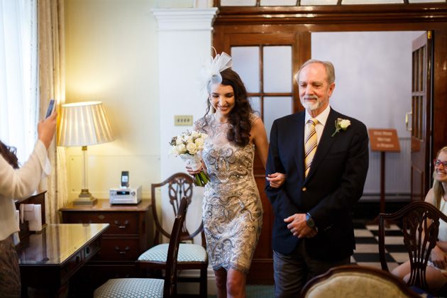 Bride in a short detailed wedding dress with white fascinator walking down the aisle with her father | Confetti.co.uk