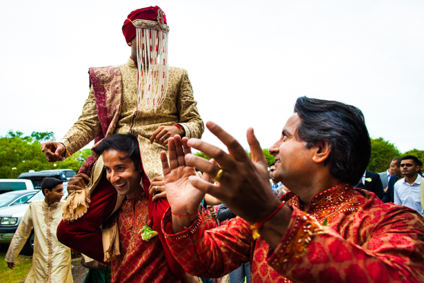 Indian groom in traditional gold and red sherwani arriving at the ceremony with the baraat| Confetti.co.uk