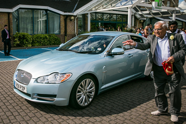 The bride and groom leaving the wedding ceremony in a blue Jaguar | Traditional Hindu wedding | Confetti.co.uk