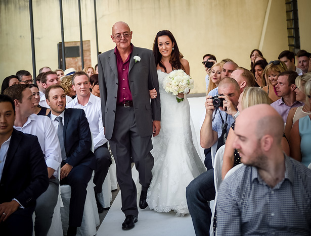 Bride in her staples lace Pronovias dress, walking down the aisle with her father | Morgan and James Real Wedding By Infinity Weddings | Confetti.co.uk