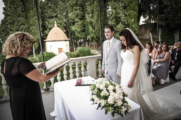 Bride in white strapless Pronovias dress with her groom, in a grey suit with coral tie, saying their vows | Morgan and James Real Wedding By Infinity Weddings | Confetti.co.uk