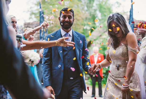 The newlyweds | Guests throwing colourful rose petal confetti over the bride and groom as they leave the church | Francesca & Arun's Fusion Real Wedding | Confetti.co.uk  