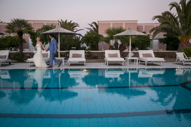 Bride and groom walking hand in hand by the pool side at the Pantheon villas Santorini| Wedding portfolio by Creative Shotz | Dasha and Steve's Real Wedding In Greece | Marryme in Greece | Confetti.co.uk