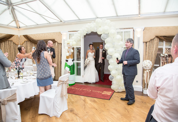 Bride and groom walking in to the reception | White balloon archway| Becki and Rob’s Real Wedding By Jenny Martin Photography | Confetti.co.uk