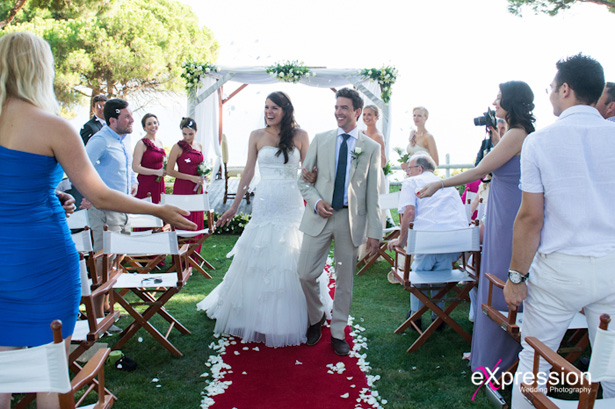 The newlyweds  walking down the aisle as guests celebrate their marriage|Wedding ceremony at the Sheraton Algarve Hotel, in the Algarve, Portugal.| Debora and James’s real destination wedding | Confetti.co.uk