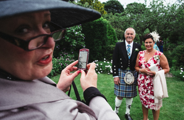 Wedding guests taking pictures of each other on their mobile phone before the ceremony  | Steph and Gary's Real Garden Wedding | Confetti.co.uk 