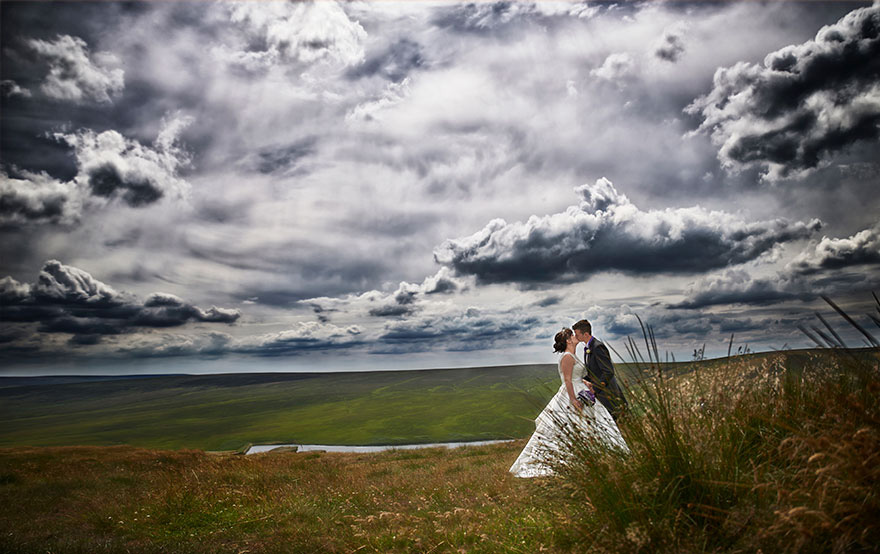 Pennine Manor Kissing Bride and Groom Couple Countryside Photo with Grey Clouds and Moody Sky | Confetti.co.uk