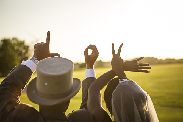 Bride and Groom Spell LOVE on Their Fingers in Front of a Sunset - Precious & Jerald’s Purple And Gold Themed Wedding | Confetti.co.uk