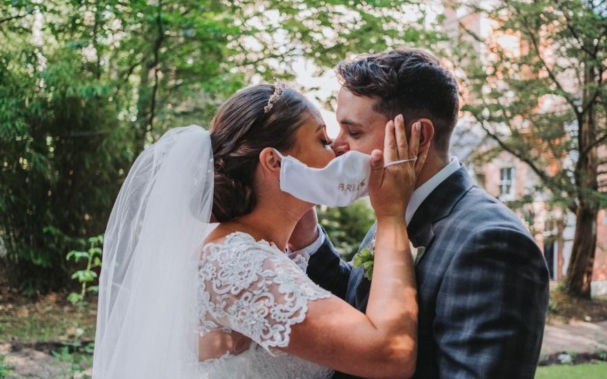 Bride and groom kissing behind face mask